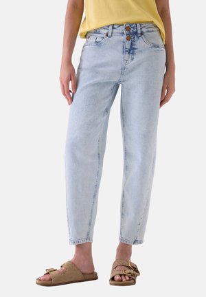 Lyseblå jeans med høj talje og to knapper, båret med en gul top og beige slip-on sandaler med dobbelte spænder.
