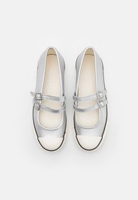 Zapatos de cuero plateado con doble hebilla, puntera redondeada y una tapa de goma blanca. El interior cuenta con una plantilla texturizada.