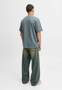 Graues Baumwoll-T-Shirt mit kurzen Ärmeln, kombiniert mit lockeren, dunkelgrünen Jeanshosen mit einem verblassten Finish und Gesäßtaschen.