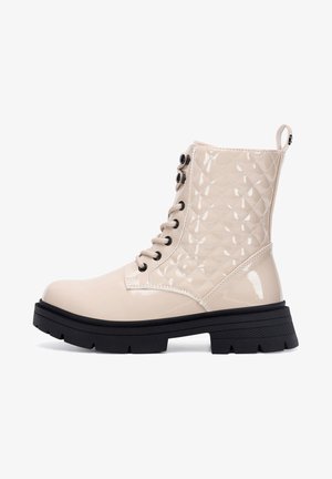 Beiger Kampfstiefel aus Lackleder mit gesteppter Oberseite, schwarzer dicker Profilsohle, schwarzen Ösen, beigen Schnürsenkeln und Zuglasche hinten.