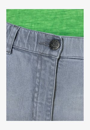 Jeans in denim grigio con chiusura a bottone, caratterizzati da una texture liscia e dettagli di cuciture sottili, su uno sfondo di camicia verde.