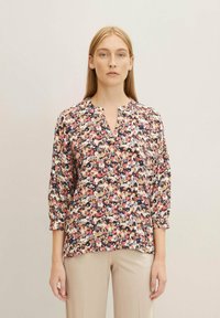 Blouse florale multicolore avec un col rond et des manches trois-quarts. Tissu léger avec une texture douce et un imprimé vibrant.