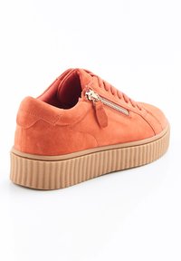 Sneaker en daim orange avec une semelle en caoutchouc épaisse et texturée, à lacets à l'avant, et un détail de fermeture éclair décoratif sur le côté.