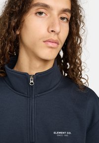 Marineblauwe quarter-zip sweatshirt met een hoge kraag, voorzien van een zilveren rits en de witte tekst "ELEMENT CO. SINCE 1992" op de borst.
