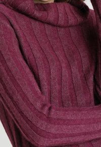 Maglione a collo alto bordeaux realizzato in tessuto morbido, con texture a coste verticali e un design del colletto avvolgente e aderente.