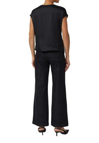 Czarna satynowa bluzka z krótkim rękawem w połączeniu z ciemnymi, szerokimi jeansami z wysokim stanem. Stylizację uzupełniają czarne sandały na obcasie.