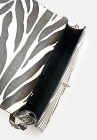 Tasche mit Zebra-Muster und strukturiertem schwarz-weißen Äußeren, ausgestattet mit einem silbernen Verschluss und einem geräumigen schwarzen Innenraum.