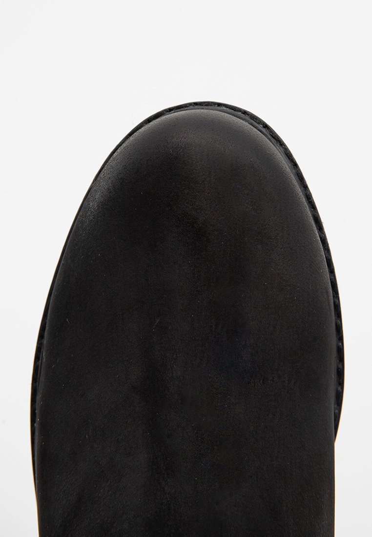 Stivale in pelle nera con punta arrotondata, texture liscia e un sottile dettaglio di cucitura lungo il bordo. La suola è leggermente rialzata.