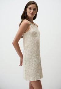 Crème-kleurige mouwloze jurk met een gestructureerd oppervlak, met een losse pasvorm en een lengte boven de knie, geschikt voor casual draagstijl.