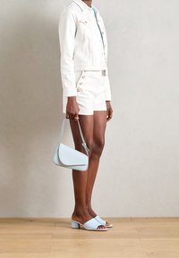 Chaqueta y shorts de mezclilla blanca con botones dorados. Bolso azul claro, sandalias tipo slide a juego con tacones de bloque. Texturas lisas.