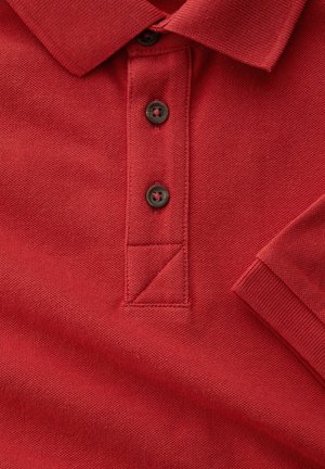 Tela de polo roja con tres botones marrones, cuello y manga corta con puño acanalado visible.