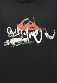 Quiksilver logo s crvenim valom i grafikom planine, bijeli istrošeni tekst "Quiksilver od 1969. Australija" na crnoj tkanini.