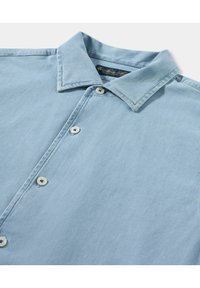 Světle modrá košile na knoflíčky vyrobená z jemné, strukturované látky, s špičatým límcem a pěti ladícími knoflíky podél légy.