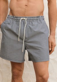 Pruhované plavky v námořnické modři a bílé, s elastickým pasem se šňůrkou, bočními kapsami a volným střihem.