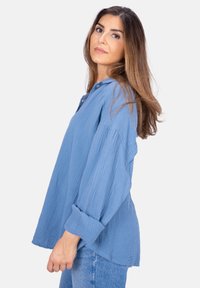 Hellblaue, strukturierte Baumwollbluse mit Kragen, langen Ärmeln und lockerem Schnitt. Verfügt über einen Knopfdetails am Halsauschnitt.