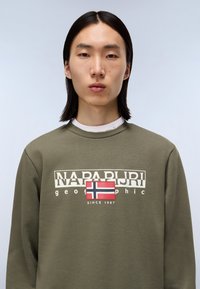 Olivengrøn sweatshirt med et hvidt logo med "NAPAPIJRI" og et norsk flagg grafik i midten, rund halsudskæring og blød tekstur.
