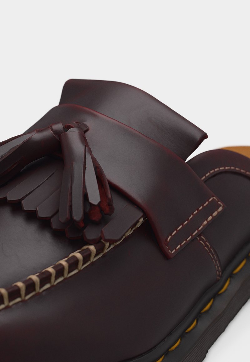 Dunkelbrauner Lederloafer mit Quasten, sichtbaren Nähten und gelb akzentuierter Sohle vor weißem Hintergrund.