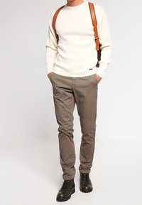 Kremowy sweter z dzianiny, brązowe spodnie w wzory oraz czarne, sznurowane botki. Brązowe szelki na swetrze dodają szczegółów do stroju.