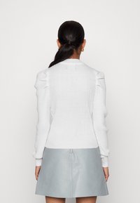 Pull blanc côtelé avec manches bouffantes, silhouette ajustée et encolure ronde, associé à une jupe en cuir bleu clair avec une fermeture éclair centrale.
