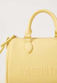 Borsa in pelle gialla con texture, dalla forma arrotondata, con manici doppi e lettering in rilievo. Presenta una tracolla rimovibile e dettagli in hardware dorato.