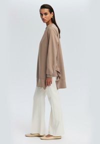 Beige dlouhý rukáv top s nařasenými detaily na rukávech, spárovaný s bílými širokými kalhotami a světlými balerínami. Jednoduchý, uvolněný střih.