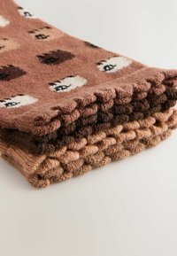 Stapel gebreide items in warme tinten met een speelse berenpatroon, die ingewikkelde texturen en patronen tonen op een lichte achtergrond.