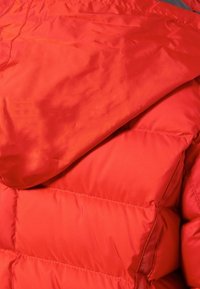 Doudoune rouge au tissu lisse, dotée d'une capuche, d'un design matelassé et de détails élastiques le long de l'ourlet et des poignets.