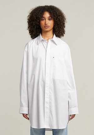 Weißes Hemd mit Knöpfen, im lässigen Schnitt, mit Kragen, langen Ärmeln, einer Tasche auf der linken Brust und minimalistischen Designelementen.