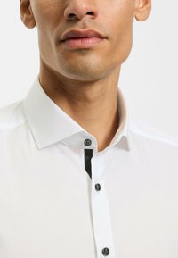 Weißes Hemd mit klassischem Kragen, schwarzer Knopfleiste und glänzenden schwarzen Knöpfen. Glattes Gewebe mit eleganter Textur.