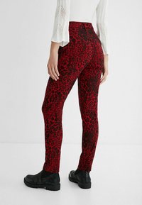 Rode en zwarte leopardprint stretchbroek met een hoge taille, gedragen met zwarte enkellaarzen. Het materiaal lijkt glad met een getailleerd ontwerp.