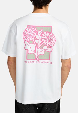 White t-shirt featuring a pink floral graphic design on the back, with the text "THE BALANCE OF OPPOSITES" beneath the illustration.