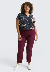 Blusa de manga corta en estampado floral navy combinada con pantalones tailoring burdeos. La modelo lleva zapatillas blancas y está de pie sobre un fondo claro.