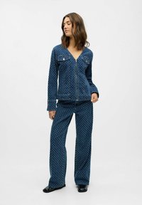 Conjunto de denim que incluye una chaqueta con cremallera y pantalones de pierna ancha, ambos en azul profundo con un sutil patrón floral. La chaqueta tiene bolsillos delanteros.