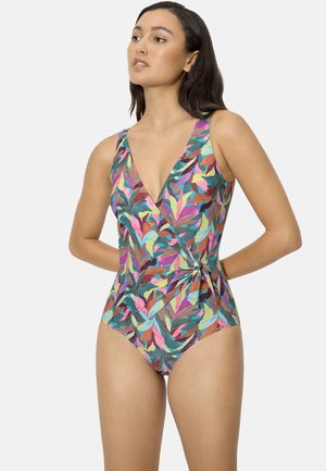 Mujer con un traje de baño de una pieza sin mangas, con estampado de hojas tropicales multicolores, escote en V y detalle de lazo en el costado.