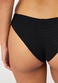 Czarne majtki bikini z teksturowanym, wzorzystym wzorem, o wysokim kroju nogawki i umiarkowanym zakryciu z tyłu.