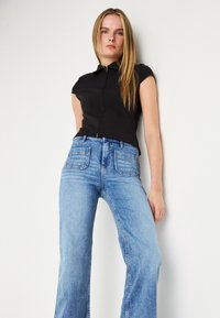 Črno zip-up kratkoleten top, ki ga kombiniramo z visokim pasom svetlo modrimi denim flared hlačami, ki imajo dva zadnja žepa in izbledel videz.