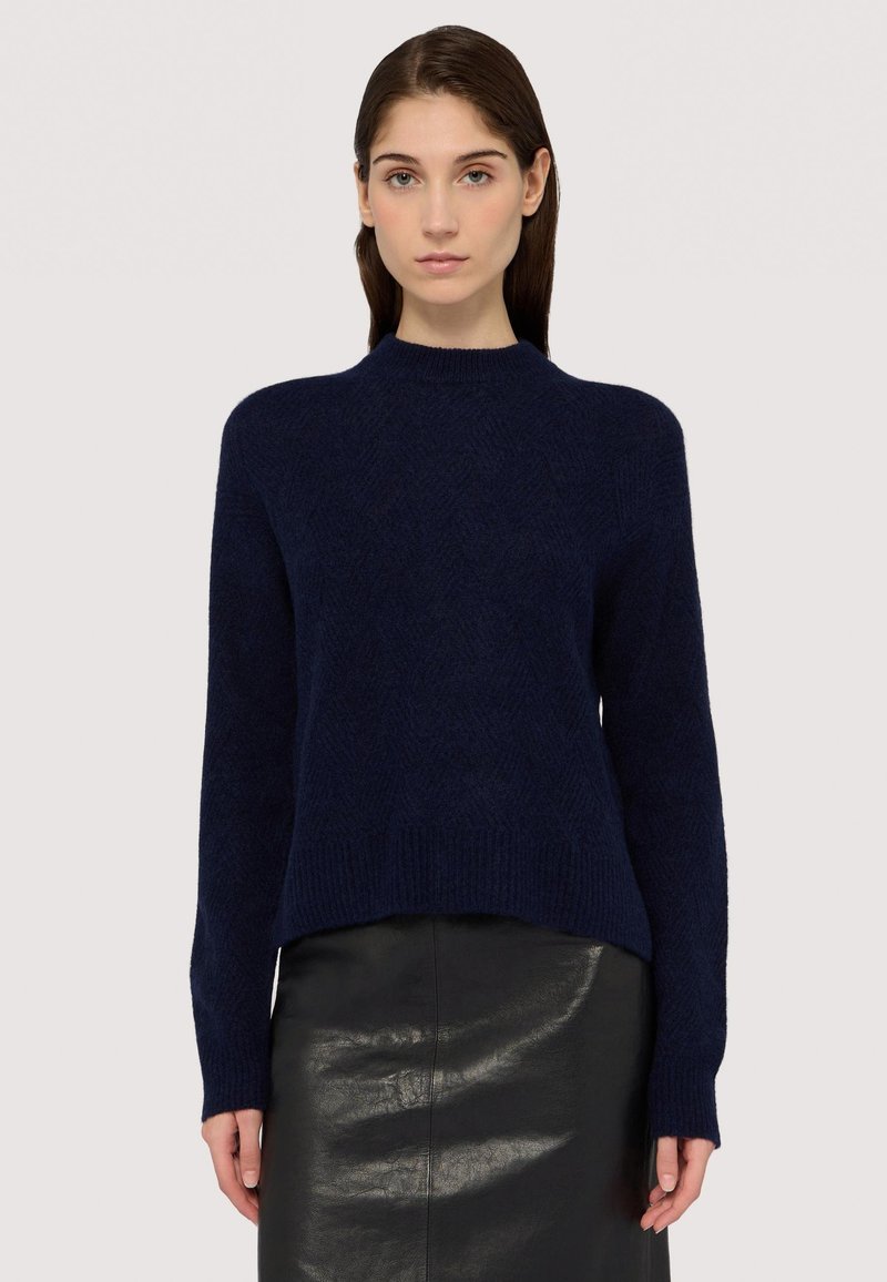 Marinblå stickad tröja med rund halsringning, långa ärmar och ett strukturerat fiskbensmönster, tillsammans med en svart läderkjol.