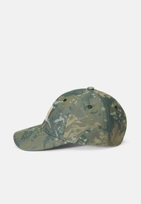 Gorra de béisbol de camuflaje hecha de tela texturizada, con visera curvada y una correa ajustable en la parte trasera. Acentuada con un parche de logo.