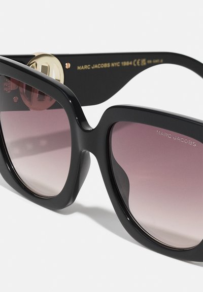 Schwarze übergroße Sonnenbrille mit einem eleganten Kunststoffrahmen, verlaufenden Gläsern, die von dunkel zu hellrosa verblassen, und einem goldenen Akzent am Bügel.