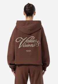 Sudadera grande marrón con una textura suave, que presenta el texto gráfico "Values & Visions" en color claro en la parte posterior. Incluye capucha ajustable.