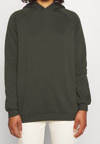 Ciemnozielona bluza z kapturem z raglanowymi rękawami, ściągaczami na mankietach i na dole. Wykonana z miękkiego materiału o gładkiej fakturze.