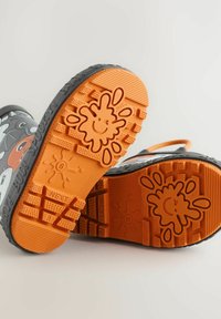 Bottes de pluie en caoutchouc noir avec des semelles orange, ornées de motifs amusants de projections. Les semelles sont dotées de grips texturés pour plus d'adhérence.