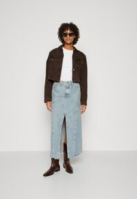 Brun cropped denim-jakke over en hvit skjorte, parret med et lys blått denim-skjørt med høy slitt og geometriske søm detaljer, samt brune ankelstøvler.