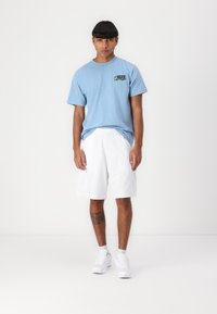 Light blue cotton t-shirt with a graphic logo on the chest, paired with white mesh shorts and white athletic sneakers.