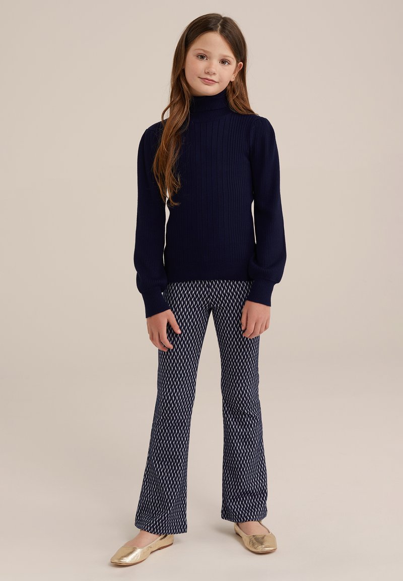 Jūras zila ribota turtlenecka džemperis apvienots ar platām, rakstainām biksēm un zelta baleta dzīvoklīšiem; gluda tekstūra un īsās piegriezuma dizains.