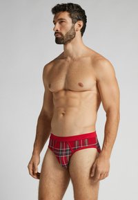 Červené kostkované slipy s jednobarevným červeným pasem, vyrobené z měkké látky. Mají klasický střih a kostkovaný vzor s kontrastními barvami.