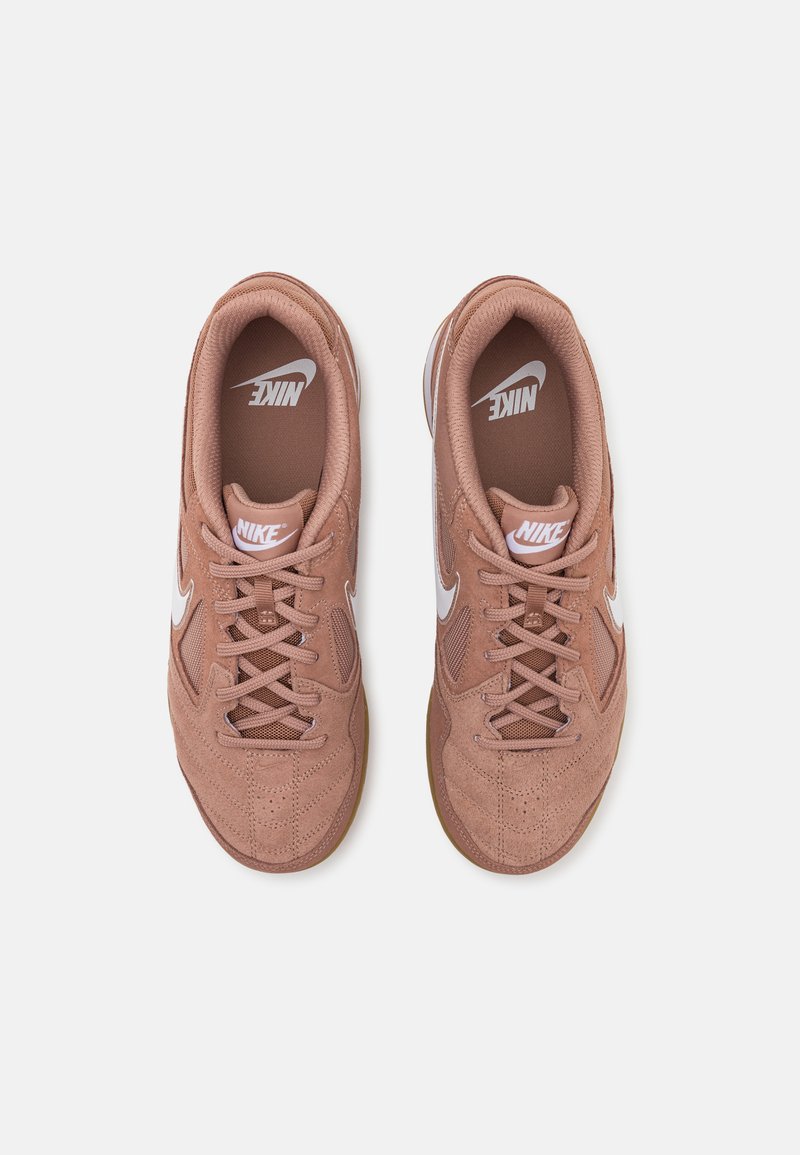 Zapatillas Nike en rosa polvo, con una parte superior de ante, detalles de malla, logo blanco y suela de goma marrón. Diseño con cordones y cuello acolchado.