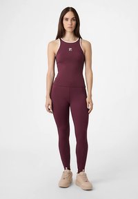 Bordeauxrotes Sporttanktop mit weißen Akzenten, kombiniert mit passenden Leggings. Glatte Textur, figurbetontes Design. Cremefarbene Sneaker vervollständigen das Outfit.