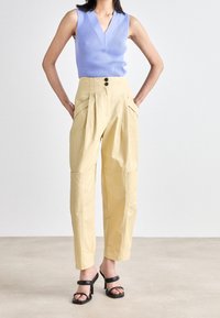 Pantaloni su misura giallo chiaro con vita alta, tasche laterali e doppi bottoni; abbinati a un top a canotta aderente in lavanda a coste. Sandali neri con tacco.