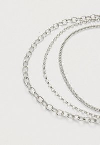 Drie zilveren kettingen met verschillende schakels: een dikke ovale schakelketting, een delicate ronde schakelketting en een gedraaide touwketting.